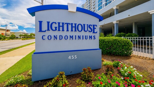 Schild für Lighthouse Condominiums mit freiem Blick auf den Eingangsbereich und eine bepflanzte Grünfläche mit Blumen.
