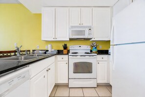 Une cuisine avec des meubles blancs, un four à micro-ondes, une cuisinière et un réfrigérateur.