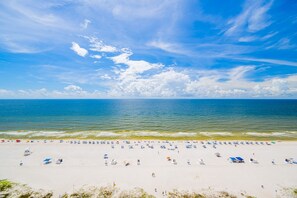 A beach with a clear sky, calm sea, and numerous umbrellas and beach chairs.