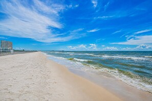 Une plage avec un ciel dégagé, un rivage sablonneux et un bâtiment en arrière-plan.