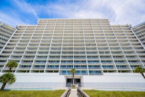 A high-rise hotel with multiple balconies, a central entrance, and a clear sky.