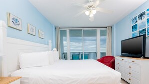 Ein Schlafzimmer mit Bett, Fernseher, einem roten Sessel und einem Balkon mit Blick zum Himmel.