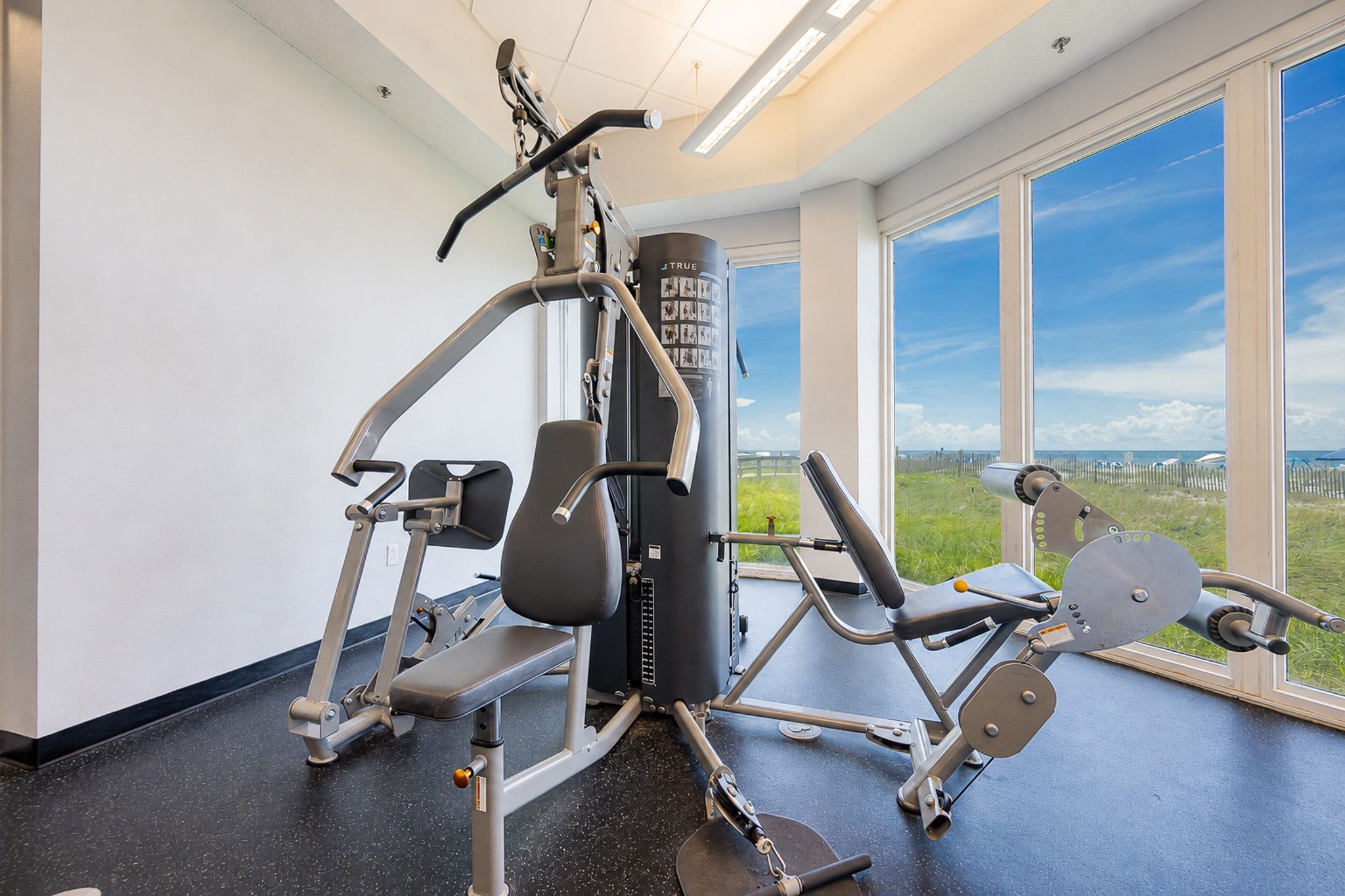 Un gimnasio con equipo de ejercicio, ventanas amplias y vistas al exterior.