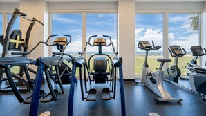 Ein Fitnessstudio mit unterschiedlichen Trainingsgeräten, großen Fenstern und Blick auf den Strand.