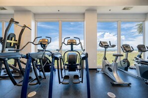 Un gimnasio con diversos equipos de ejercicio, ventanas amplias y vistas a la playa.