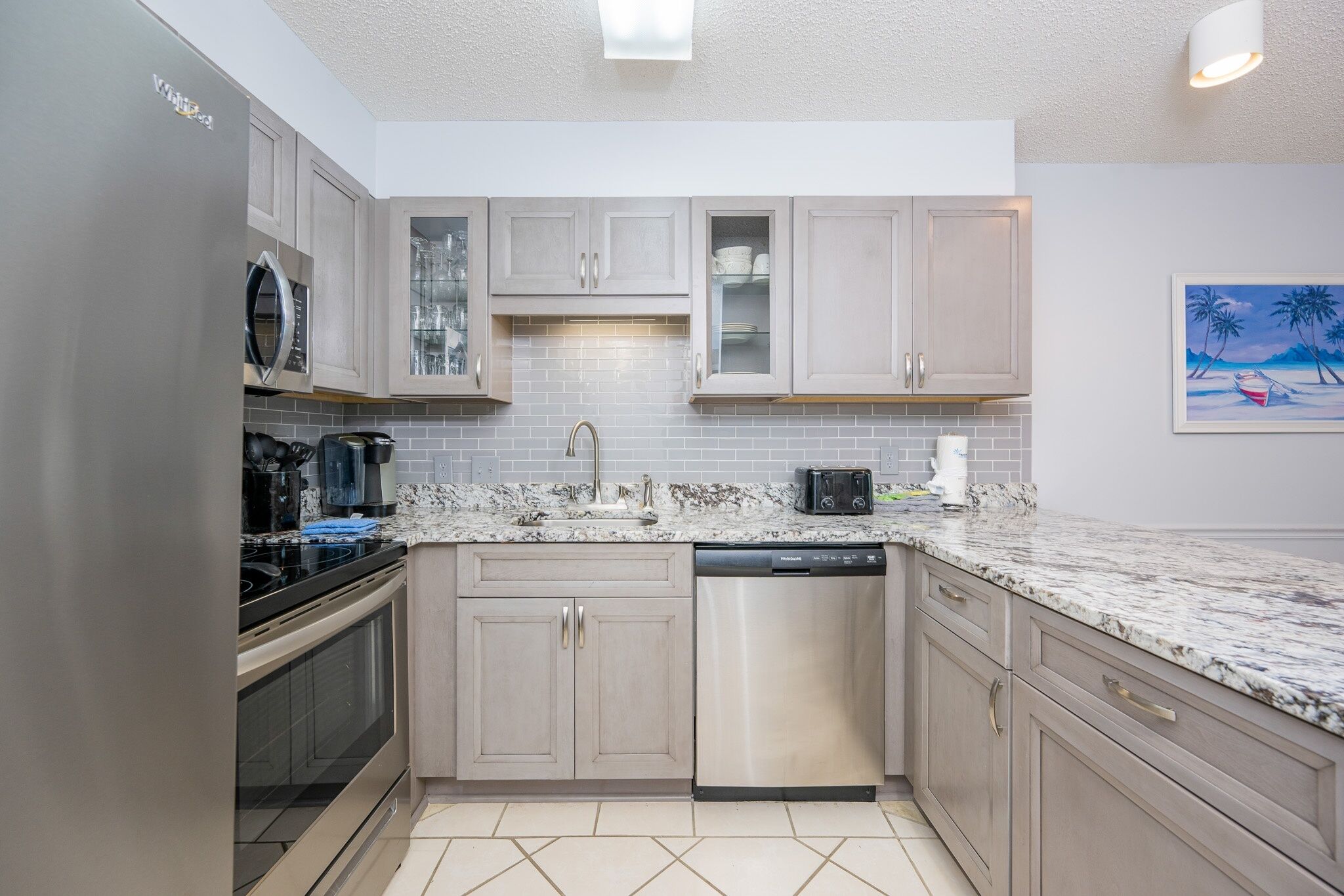 A modern kitchen with light wood cabinets, a stainless steel dishwasher, and a granite countertop.