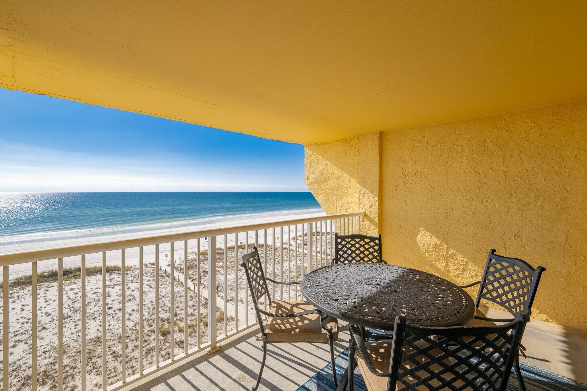 Un balcon donnant sur la plage, une table ronde avec des chaises et un mur jaune.