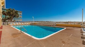 A rectangular pool with a metal ladder, surrounded by lounge chairs and a white fence.