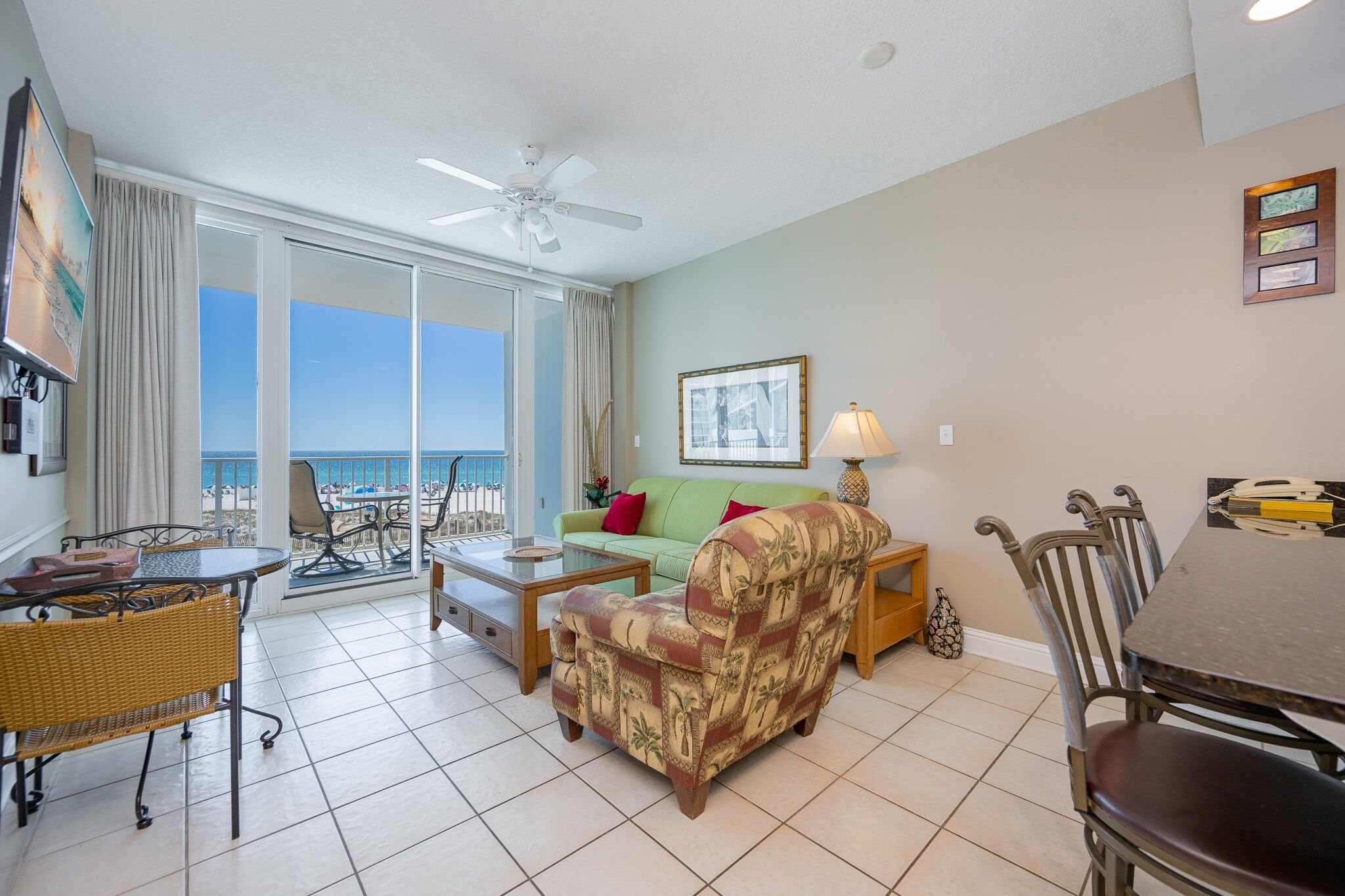 A living room with a balcony, a ceiling fan, a sofa, a coffee table, and a dining area with chairs.