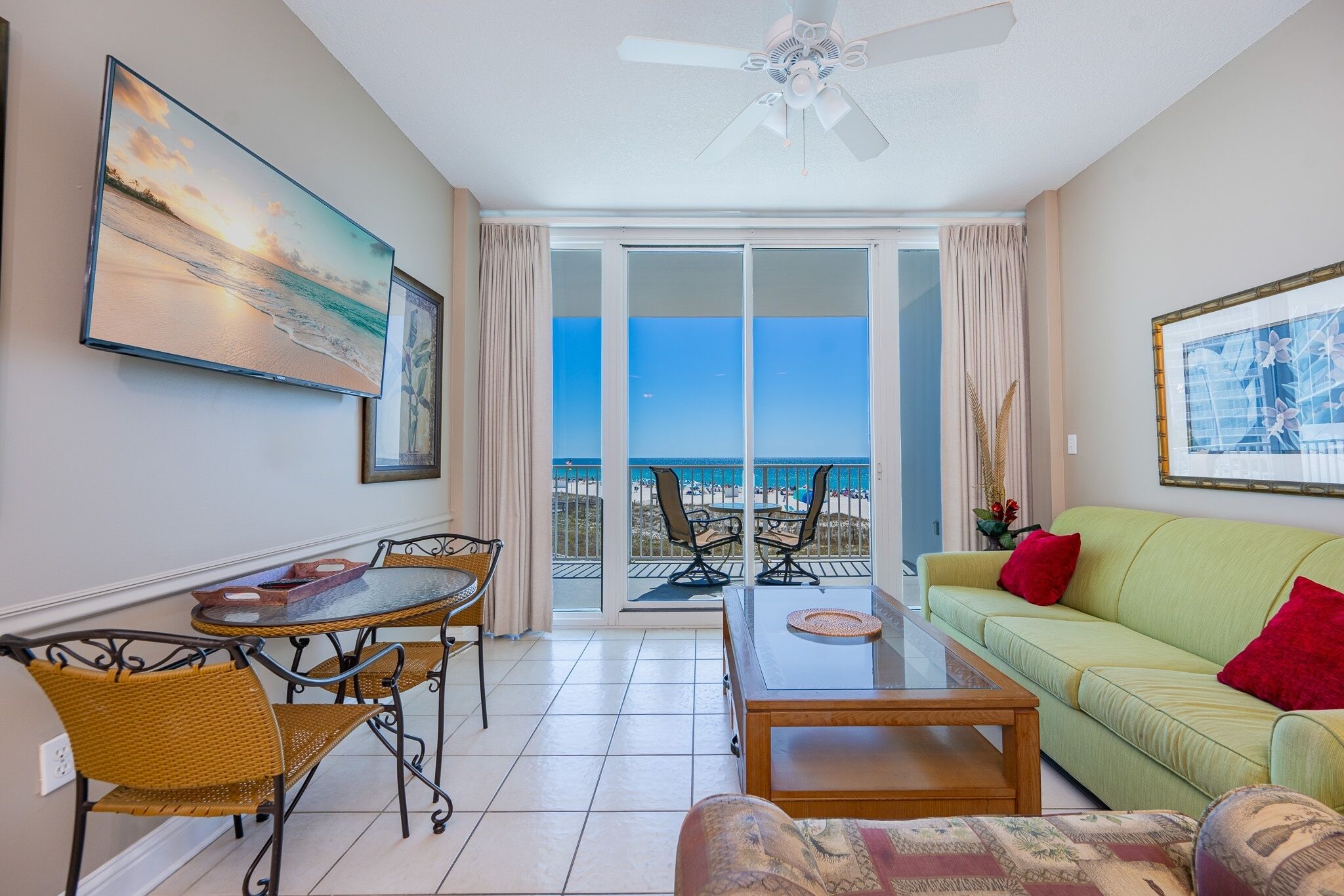 A room with a balcony, a dining table with chairs, a sofa, and a ceiling fan.