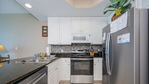 A kitchen with white cabinets, a stainless steel refrigerator, a microwave, and an oven. - Lighthouse 216 1 Bedroom Condo (Gulf Shores)