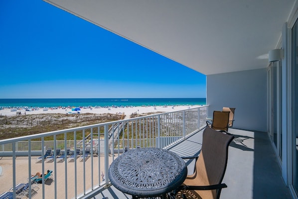 A balcony with a view of a beach, a round table, and two chairs. - Lighthouse 216 1 Bedroom Condo (Gulf Shores)