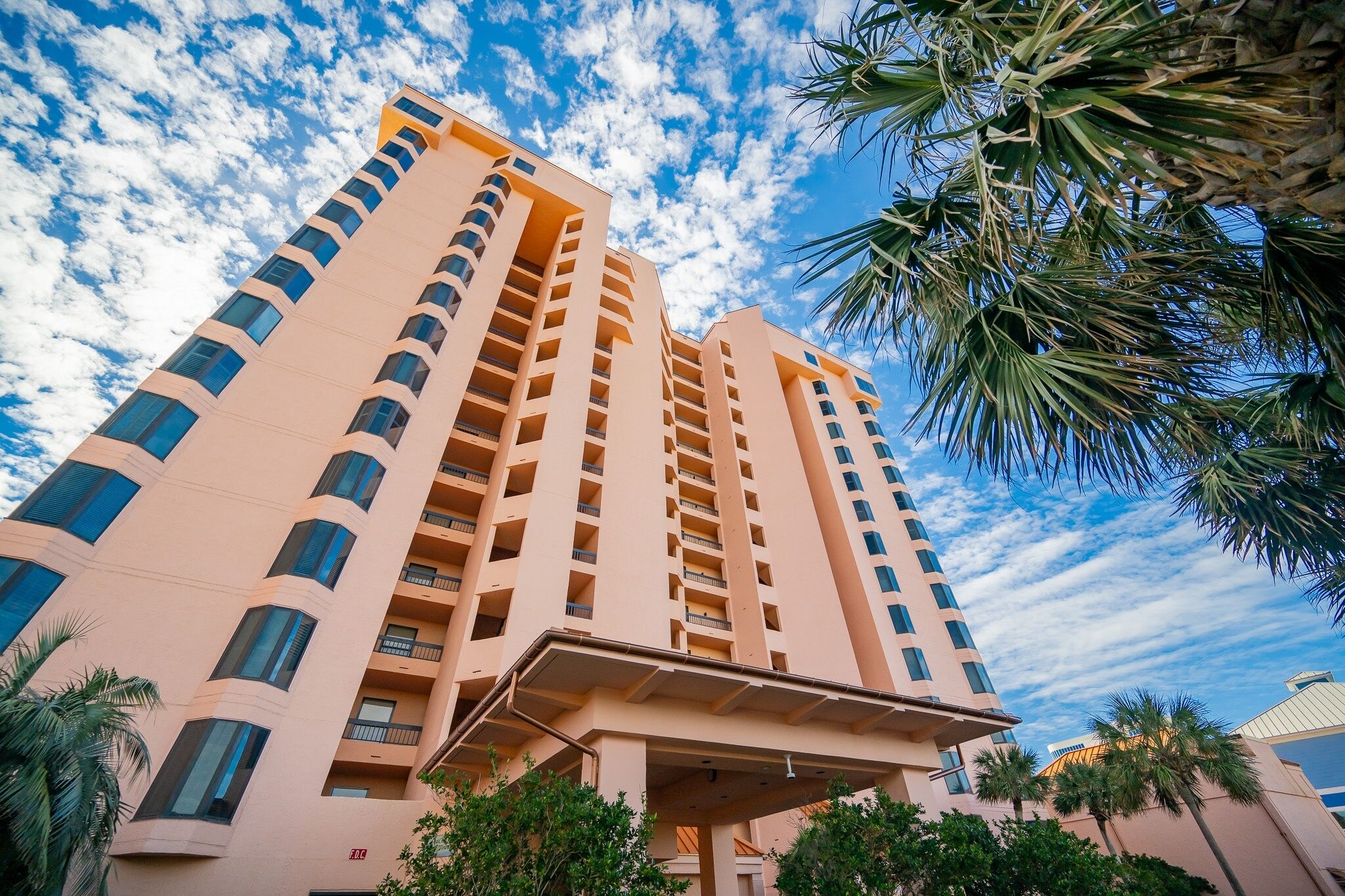 A tall, multi-story hotel with a modern design, featuring balconies on each floor and a covered entrance area.