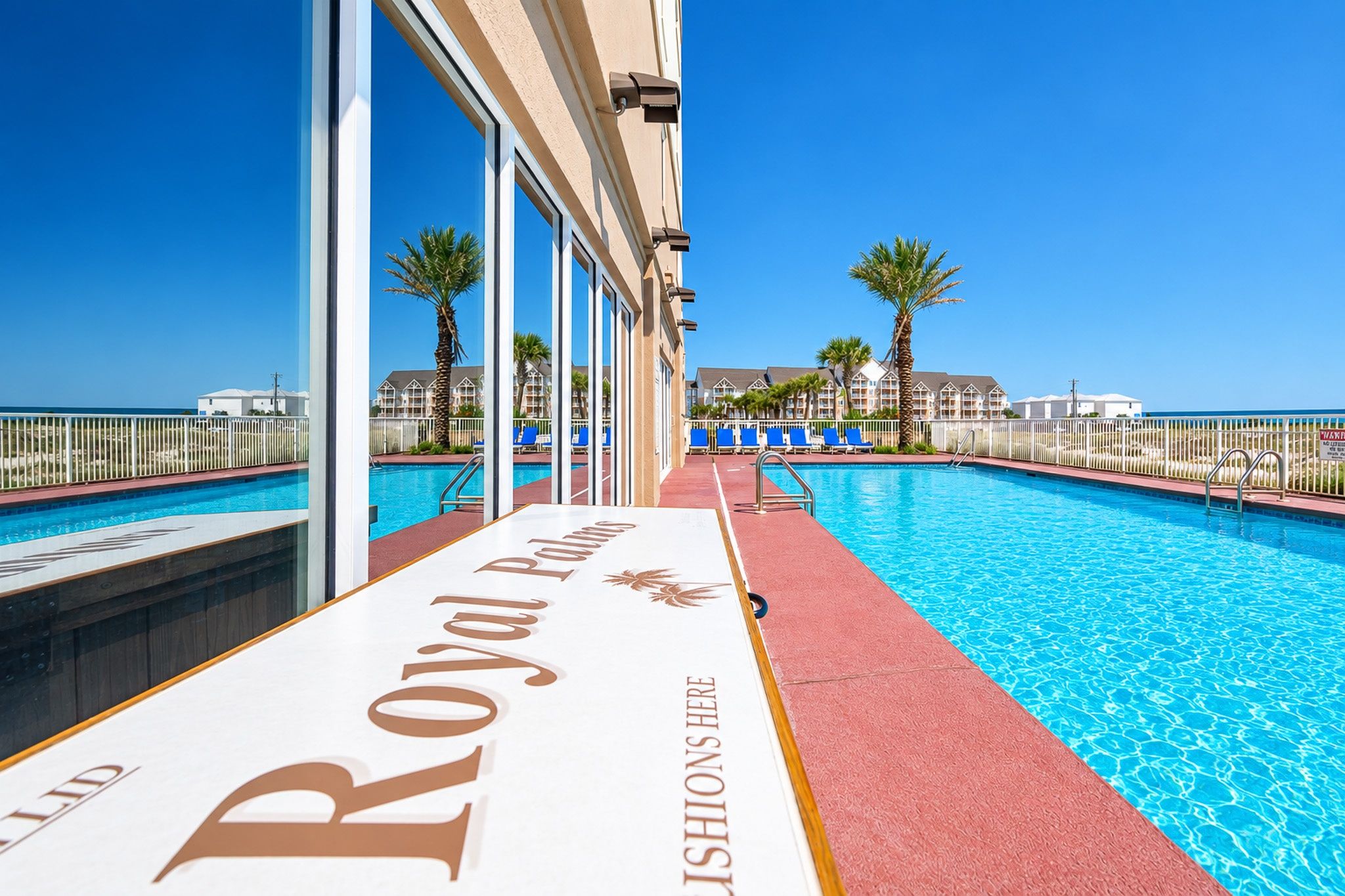 Uitzicht op het zwembad, met een bord waarop 'Royal Palm' staat en een helderblauwe lucht.