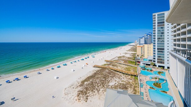 A beachside hotel with a pool area, beach umbrellas, and a clear view of the ocean.