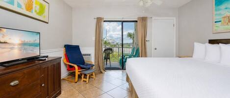 A hotel room with a bed, a TV, a chair, a ceiling fan, and a balcony with chairs.