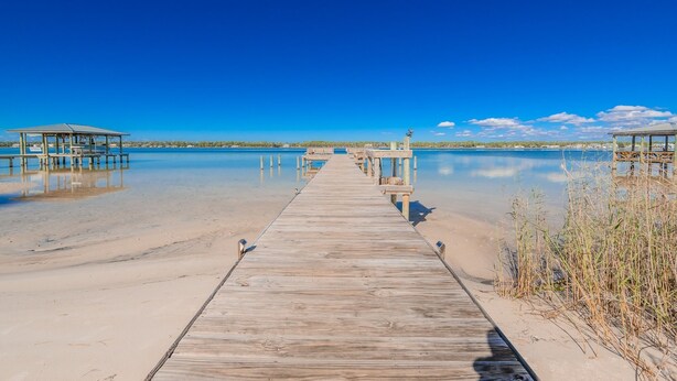 Un muelle de madera que da a una playa con agua azul cristalina y un cielo sereno.