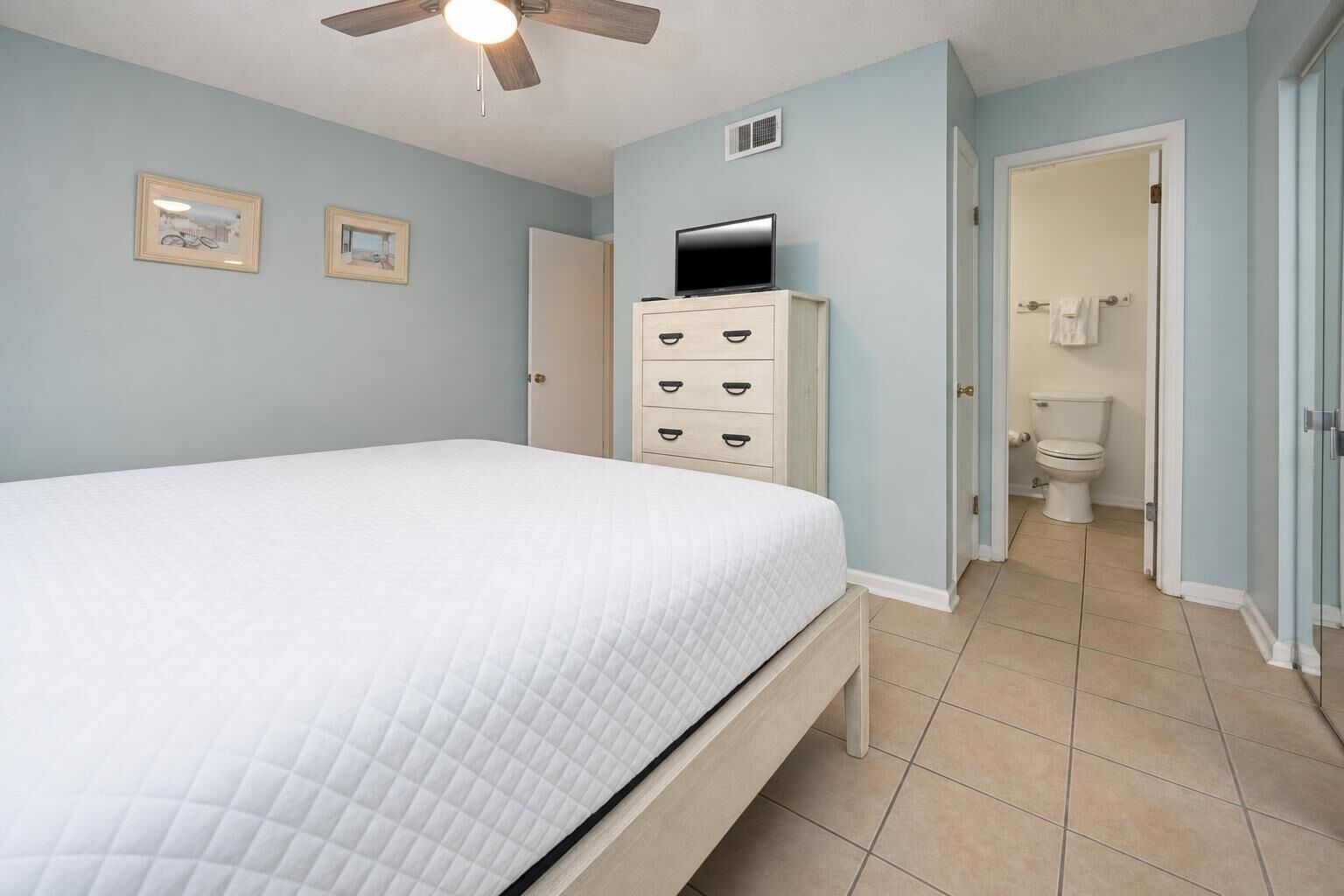 A bedroom with a bed, a dresser, a television, and a bathroom with a toilet and shower.