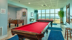 A pool table area with two pool tables, a foosball table, and a large window overlooking the beach. - Crystal Shores West 807 2 Bedroom Condo (Gulf Shores)