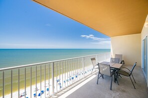 A balcony with a view of the beach and ocean, a table with chairs, and a partial view of a building. - Crystal Shores West 807 2 Bedroom Condo (Gulf Shores)