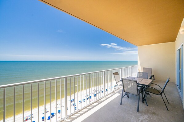 A balcony with a view of the beach and ocean, a table with chairs, and a partial view of a building.