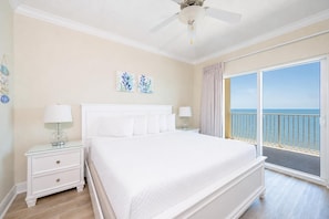 A hotel room with a bed, bedside tables, a ceiling fan, and a balcony with a view of the ocean. - Crystal Shores West 807 2 Bedroom Condo (Gulf Shores)