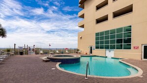 A pool area with a hot tub, lounge chairs, and a building with large windows. - Crystal Shores West 807 2 Bedroom Condo (Gulf Shores)