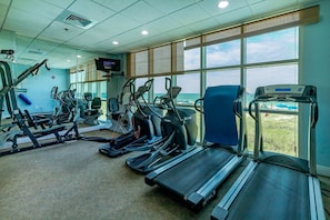 Ein Fitnessstudio mit Laufbändern, Crosstrainern und Kraftgeräten, große Fenster mit Blick auf den Strand.