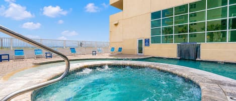 Piscina com escada de metal, cercada por espreguiçadeiras e um edifício com amplas janelas.