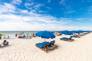 A beach with rows of blue umbrellas and wooden lounge chairs.