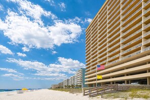 A beachfront hotel with multiple floors and balconies, a sandy beach, and a clear sky.