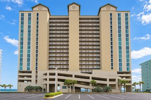 A multi-story hotel with a central atrium, parking lot, and palm trees. - Crystal Shores West 807 2 Bedroom Condo (Gulf Shores)