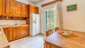 A kitchen with wooden cabinets, a refrigerator, a window with curtains, and a dining table with a tray.