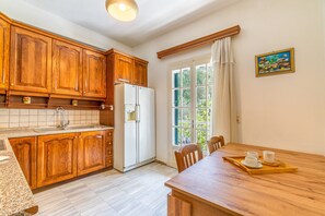 A kitchen with wooden cabinets, a refrigerator, a window with curtains, and a dining table with a tray.