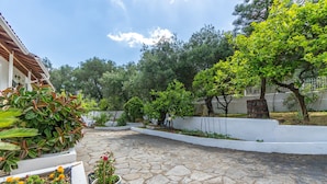 A courtyard with stone flooring, potted plants, and a white wall.