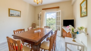 A dining area with a wooden table, chairs, a chandelier, and a vase of flowers.