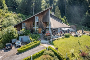 Une grande cabane en bois avec un toit en pente, une terrasse couverte et un parking.