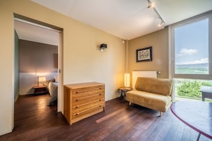 Une pièce comprenant une commode en bois, un canapé, une petite table, une lampe et une fenêtre donnant sur un beau paysage.