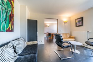 A modern living room with a sofa, chairs, a dining area, and a painting on the wall.