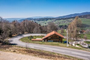 Eine ländliche Straße schlängelt sich durch eine hügelige Landschaft mit einem Holzhaus und blauem Himmel.