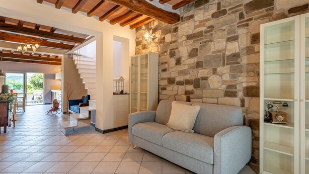 Ein Wohnzimmer mit Steinwand, grauem Sofa, Treppe und einem Glaskabinent.