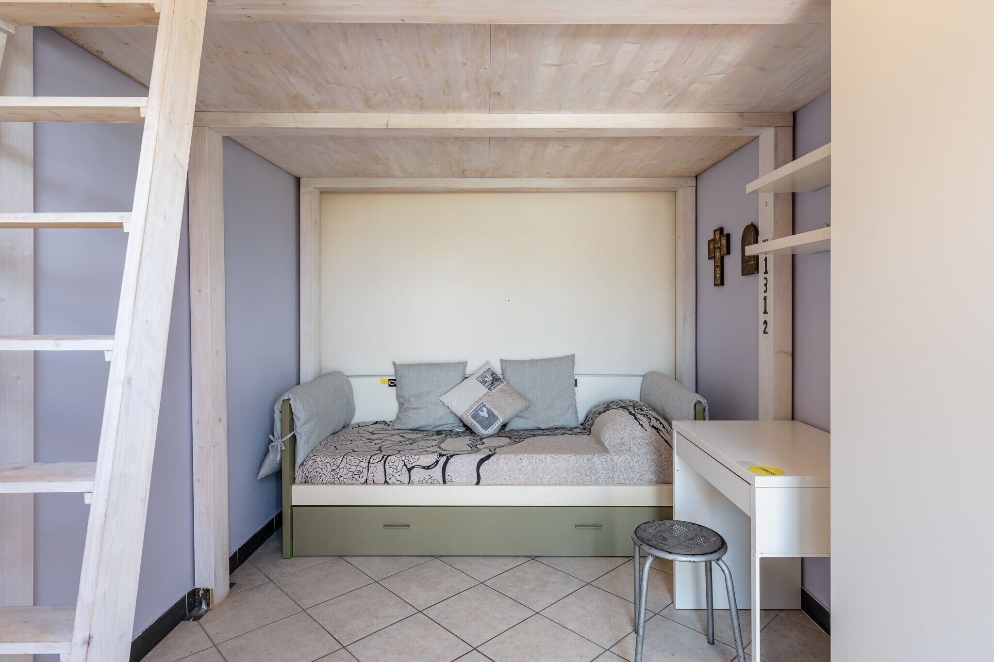 A bedroom with a bed, a desk, and a ladder.