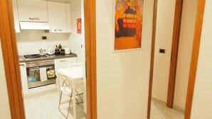 A hallway leading to a kitchen with white cabinets, a dining area with a table and chairs, and a poster on the wall. - Quiet & Cosy Colosseum (Roma)