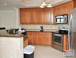 A kitchen with wooden cabinets, a microwave, stove, and a trash can.