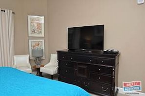A hotel room with a bed, a television on a dresser, and a framed picture on the wall.