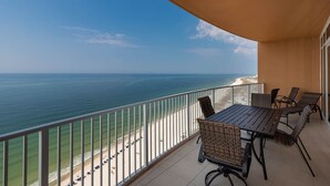 A balcony with a view of the ocean, a table, and wicker chairs.