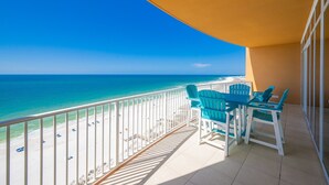 A balcony with a view of the ocean, a table with chairs, and a sunshade.