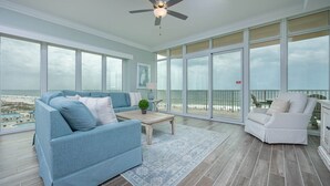 Ein geräumiger Balkon mit Blick auf den Strand, eine blaue Couch, ein weißer Sessel und ein Holztisch.