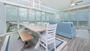 Ein geräumiger Balkon mit Blick auf Strand und Pool, ein Holztisch mit Stühlen und ein blaues Sofa.