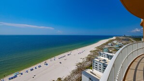 Blick auf einen Strand vom Balkon, mit blauem Himmel, Sandstrand und Gebäuden im Hintergrund.